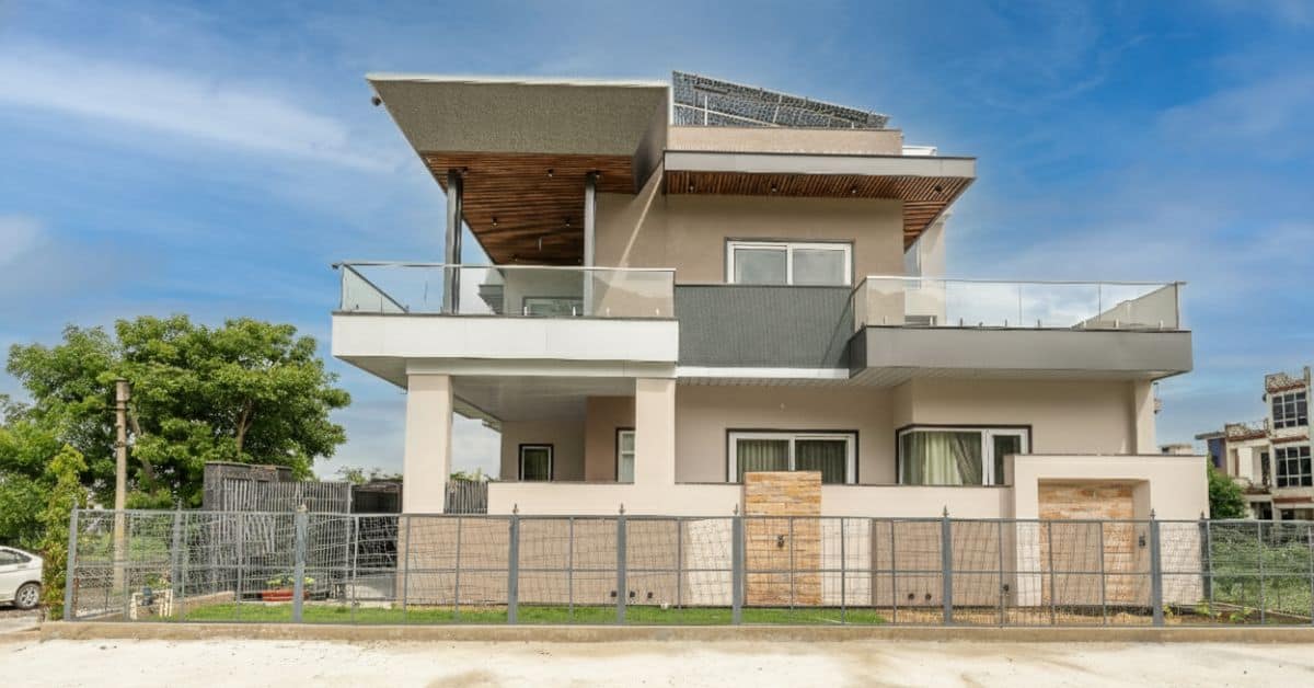 Modern two-story residential building with a beige and grey facade and glass balcony railings