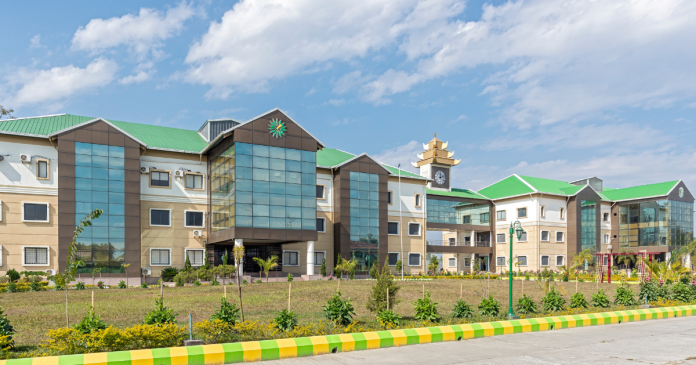Modern beige academic buildings with green roofs and a glass atrium under a blue sky.