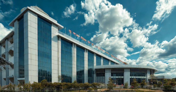 Modern glass-fronted building with a curved entrance pavilion beneath a blue sky and fluffy clouds.